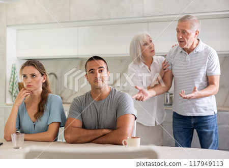 Portrait of an offended married couple in home kitchen, which mature family members reprimand. Family conflict Portrait of an offended married couple in home kitchen, which mature family members reprimand. Family conflict 117949113