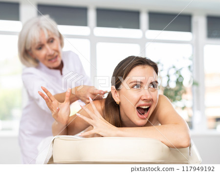 Young woman suffers painful sensations and winces during therapeutic massage session Young woman suffers painful sensations and winces during therapeutic massage session 117949192
