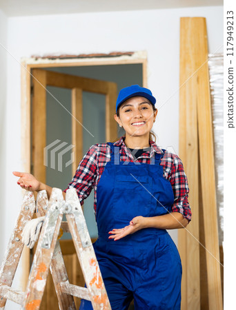 Young woman builder posing next to a stepladder in room being renovated Young woman builder posing next to a stepladder in room being renovated 117949213
