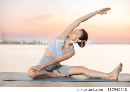 Near sea during sunset, girl performs variations of Janu Shirshasana Near sea during sunset, girl performs variations of Janu Shirshasana 117949328