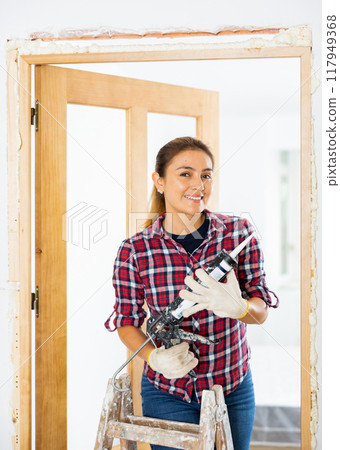 Woman herself fills the gaps with mounting foam - installation of new doors in room 117949368