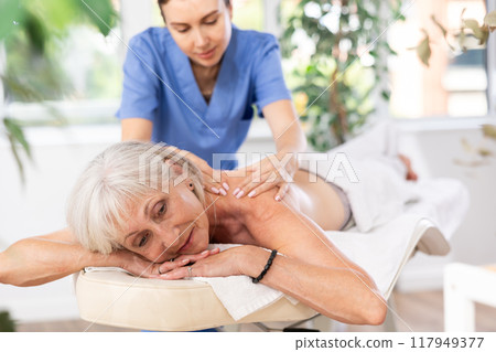 Blurry unrecognizable woman performs shoulder massage to female client. 117949377