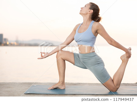 Near sea during sunset, girl performs Ardha Anjaneyasana Near sea during sunset, girl performs Ardha Anjaneyasana 117949437