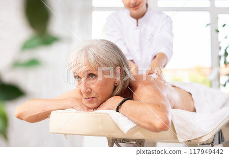 Cropped circumcised woman performs shoulder massage to female client. Cropped circumcised woman performs shoulder massage to female client. 117949442