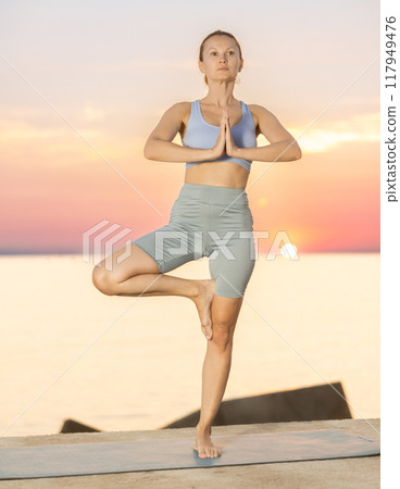 Near sea during sunset, girl performs Tiryaka Tadasana Near sea during sunset, girl performs Tiryaka Tadasana 117949476