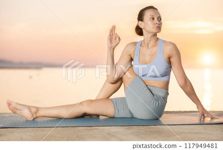 Near sea during sunset, girl performs Matsyendrasana 117949481