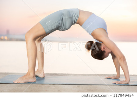 Near sea during sunset, girl performs Ardha chakrasana Near sea during sunset, girl performs Ardha chakrasana 117949484
