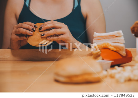 fast food, people and unhealthy eating concept - close up of woman hands holding hamburger or cheeseburger fast food, people and unhealthy eating concept - close up of woman hands holding hamburger or cheeseburger 117949522