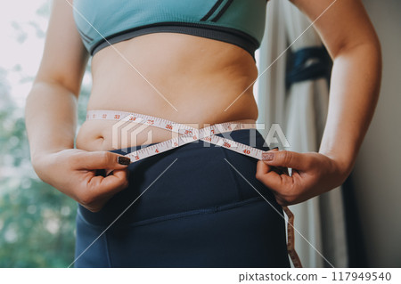 fat woman, fat belly, chubby, obese woman hand holding excessive belly fat with measure tape, woman diet lifestyle concept 117949540