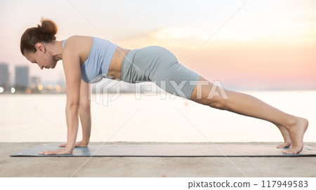 Sporty energetic experienced young woman yoga trainer performing plank pose on beach at sunrise. Fitness concept 117949583