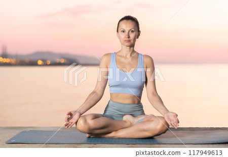 Near sea during sunset, girl performs variations of padmasana 117949613
