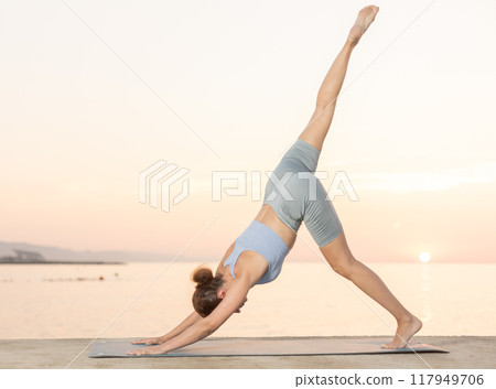 Near sea during sunset, girl performs Adho Mukha Svanasana Near sea during sunset, girl performs Adho Mukha Svanasana 117949706