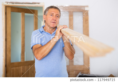 Middle-aged male carpenter in uniform holding wooden planks indoors 117949715