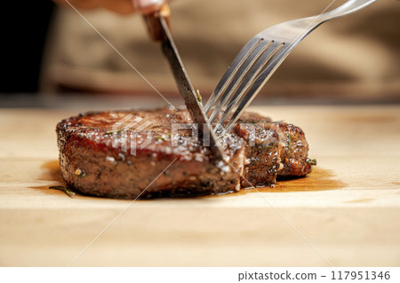 A person is cutting a piece of tenderloin meat with a knife on a wooden cutting board A person is cutting a piece of tenderloin meat with a knife on a wooden cutting board 117951346