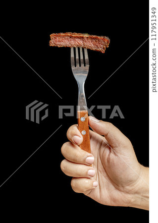 A hand holding a fork with a tenderloin piece of meat on it 117951349