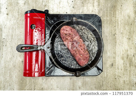 A piece of sirloin meat is cooking in a pan on a stove 117951370