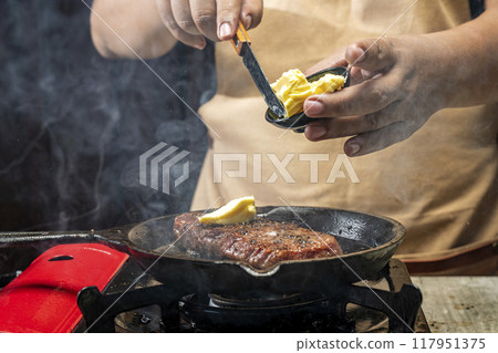 A person is cooking a sirloin steak in a pan with butter 117951375