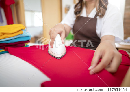 An Indonesian housewife is ironing a pile of clothes 117951434
