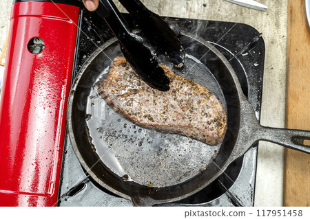 A person is cooking a picanha steak in a pan on a stove 117951458