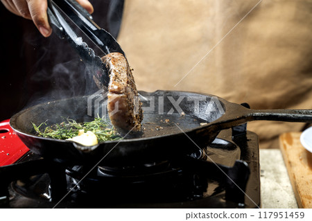 A person is cooking a picanha steak in a pan on a stove 117951459