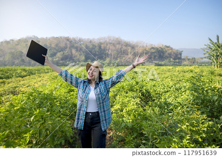 An Indonesian farmer girl is holding a tablet and smiling in a field of chili plants An Indonesian farmer girl is holding a tablet and smiling in a field of chili plants 117951639