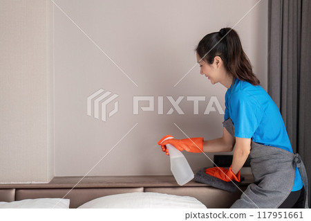 Housekeeper spraying cleaner on bedroom shelf for dusting Housekeeper spraying cleaner on bedroom shelf for dusting 117951661