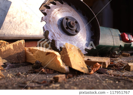Circular saw blade cutting through logs with wood shavings and debris in a rustic workshop setting Circular saw blade cutting through logs with wood shavings and debris in a rustic workshop setting 117951767