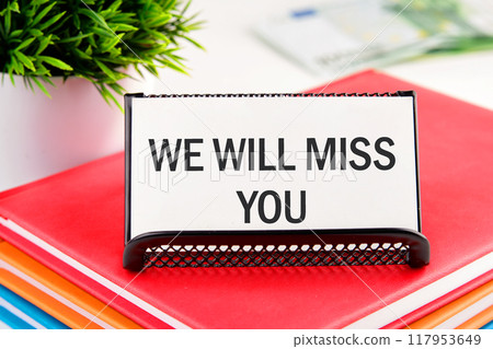 WE WILL MISS YOU written on a business card standing in a stand on notebooks 117953649
