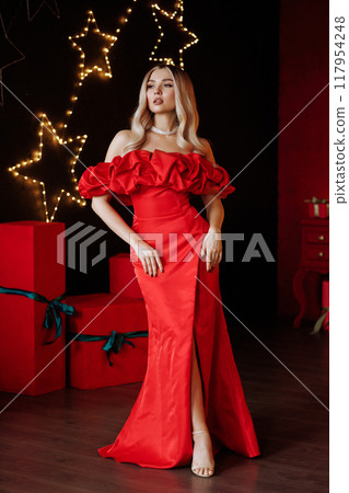 A woman in a red dress stands in front of a Christmas tree. Full length. A woman in a red dress stands in front of a Christmas tree. Full length. 117954248