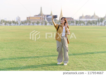 Traveler asian woman in her 30s take a livestream on smartphone while explores Wat Phra Kaew emerald Buddha. Share the wonders of Thai heritage through her journey. 117954667