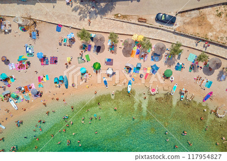 Sea beach with colorful umbrellas and relaxing people, aerial top view. Crowded sandy beach at high season. Tourists at summer holidays in Croatia 117954827