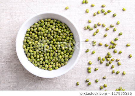 Mung beans, green gram in a white bowl on linen fabric. Dried seeds of Vigna radiata, a member of the legume family Fabaceae, used as an ingredient in both savoury and sweet dishes in Asian cuisine. 117955586