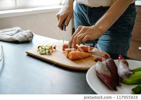 Hands of unrecognizable woman slicing carrot on chopping board, close-up view Hands of unrecognizable woman slicing carrot on chopping board, close-up view 117955928