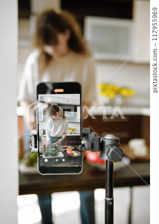 Smartphone recording a focused woman preparing food in a modern kitchen Smartphone recording a focused woman preparing food in a modern kitchen 117955969