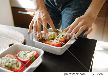 Close-up of female hands arranging stuffed bell peppers in baking tray 117955973
