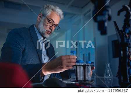 Scientist in the laboratory holding test tubes and intently looking at its contents 117956287