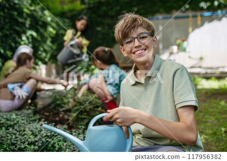 Portrait of schoolboy taking care of plants in school garden during at outdoor sustainable education class. Concept of experiential learning and ecoliteracy. 117956382