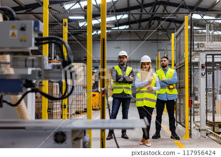 Portrait of team of warehouse employees standing in warehouse. Team of workers and female manger in modern industrial factory, heavy industry, manufactrury. Concept of team management. Portrait of team of warehouse employees standing in warehouse. Team of workers and female manger in modern industrial factory, heavy industry, manufactrury. Concept of team management. 117956424