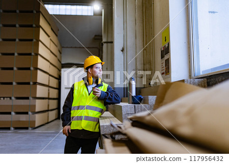Worker with Down syndrome having break in factory, warehouse, drinking coffee from thermos. Concept of workers with disabilities, support in workplace. Worker with Down syndrome having break in factory, warehouse, drinking coffee from thermos. Concept of workers with disabilities, support in workplace. 117956432