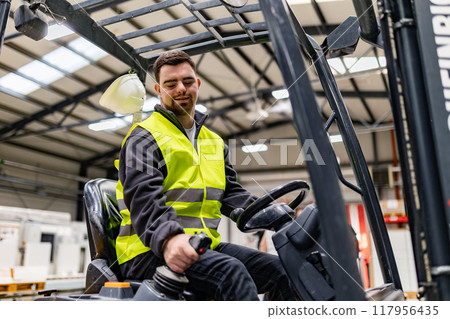 Portrait of young man with Down syndrome driving forklift, working in factory, warehouse. Concept of workers with disabilities, support in workplace. Portrait of young man with Down syndrome driving forklift, working in factory, warehouse. Concept of workers with disabilities, support in workplace. 117956435