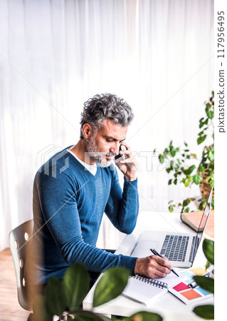 Man phone calling and writing notes in planner, working at desk from home. Telecommuting and home office. 117956495