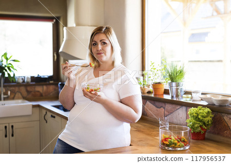 Portrait of beautiful young overweight woman choosing healthy food, eating vegetable salad. Beauty and body positivity concept. 117956537