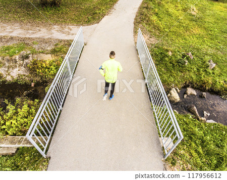 Aerial view of a runner running across bridge in park on a jogging path. Morning running training. Aerial view of a runner running across bridge in park on a jogging path. Morning running training. 117956612