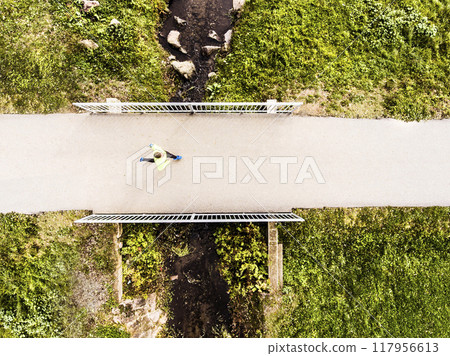 Aerial view of a runner running across bridge in park on a jogging path. Morning running training. 117956613