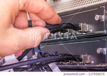 Hand of computer technician connecting fiber optics cable into data switch Hand of computer technician connecting fiber optics cable into data switch 117956679