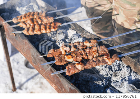 Tasty grilled meat on metal skewers on the brazier in winter. 117956761