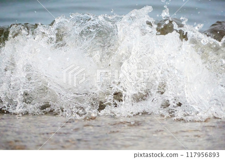 White foam and sea water drop splashes slow motion with sand and blue water 117956893
