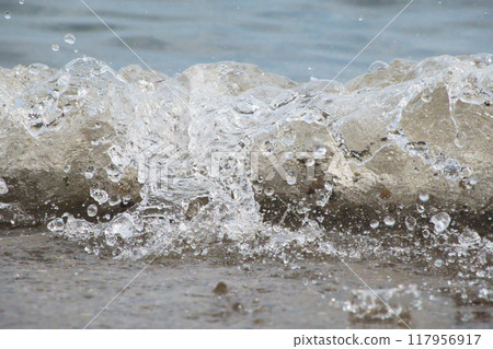 White foam and sea water drop splashes slow motion with sand and blue water 117956917