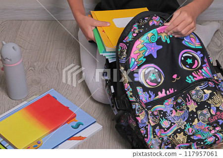 Schoolgirl in uniform black dress sit on floor collecting school bag. Free space, background for design, text. Back to school.  117957061