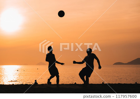 Silhouettes of Asian men playing beach soccer on beach by sea at sunrise 117957600